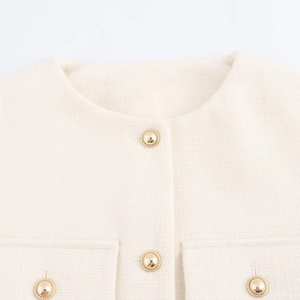 Detailed macro view of cream-colored tweed fabric texture and gold embossed buttons