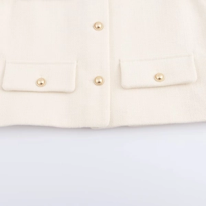Close-up of cream tweed jacket featuring embossed gold buttons and flap pocket details
