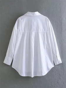 Detail showing the back pleats and curved hem of a white long-sleeved poplin shirt