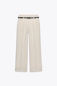 Dettaglio dei pantaloni a gamba larga crema con pieghe frontali e cintura nera sottile