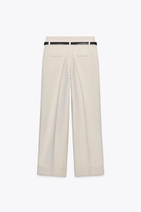 Dettaglio dei pantaloni a gamba larga color crema a vita alta con sottile cintura nera