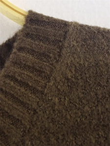 Detail view of brown knit sweater texture featuring ribbed cuff and soft wool blend fabric