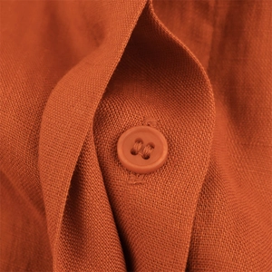 Macro detail of linen fabric texture with a color-matched round button on orange trousers