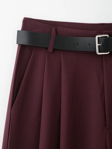 Dettaglio dei pantaloni bordeaux con doppie pieghe e cintura nera con fibbia argentata