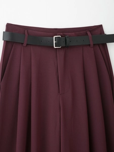 Dettaglio di pantaloni bordeaux a vita alta con doppie pieghe e cintura sottile in pelle