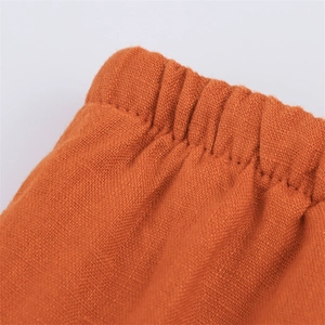 Macro detail of elastic waistband and pleated texture on orange linen wide leg pants