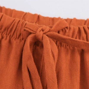 Detail of caramel linen trousers featuring an elastic pleated waist and a fabric tie knot