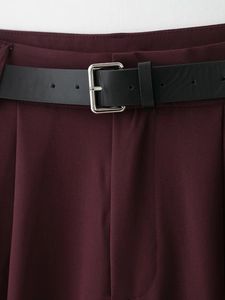 Dettaglio dei pantaloni rosso vino con doppie pieghe e cintura nera in ecopelle