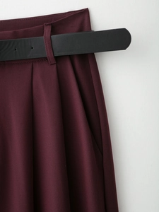 Dettaglio di pantaloni bordeaux a pieghe con trama in twill fine e cintura nera sottile