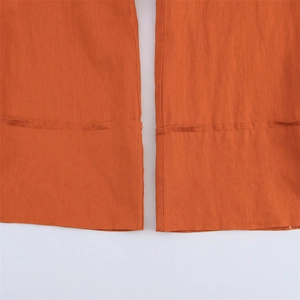 Detailed close-up of orange linen wide-leg trousers showing fabric texture and hem stitching