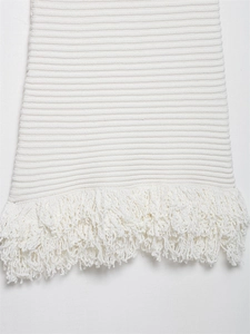 Detailaufnahme des weißen Strickkleids mit markantem Fransenabschluss und Rippenmuster