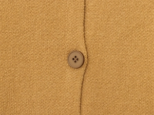 Dettaglio di un bottone in resina marrone su un cardigan in maglia boucle color cammello