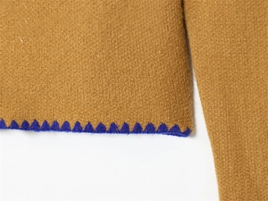 Dettaglio macro di maglieria marrone con ricamo blu a dente di sega sul bordo inferiore