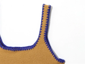 Dettaglio del top in maglia con bordi all'uncinetto blu a contrasto su tessuto giallo senape