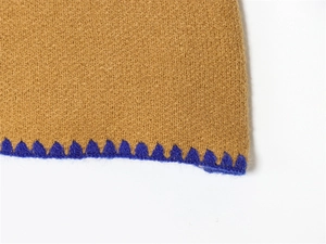 Vista macro di maglia color cammello con bordo all'uncinetto smerlato blu vivace