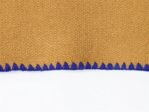Dettaglio del tessuto marrone con cuciture decorative a zig-zag blu scuro sul bordo