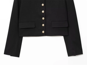 Detail of elegant black cropped blazer with gold embossed buttons and flap pockets