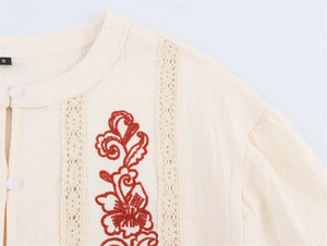 Close-up of beige cotton linen shirt featuring red floral embroidery and lace details