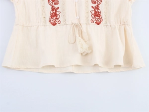 Detail of red floral embroidery and drawstring waist with tassels on linen shirt