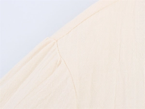 Macro view of shoulder seam and pleated sleeve detail on a cream linen shirt
