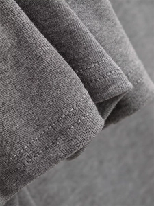 Detailed close-up of grey knitted fabric texture and neat double-needle hem stitching