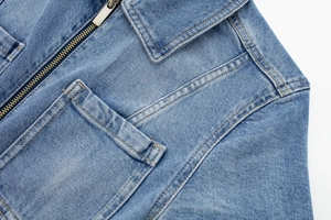 Détail d'une veste en jean bleu clair montrant le col classique et la fermeture éclair en métal