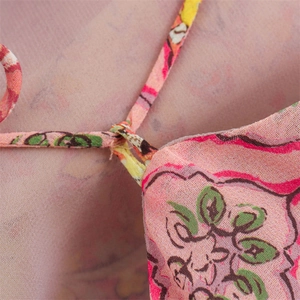 Detail of floral print fabric with thin shoulder strap on a peach pink summer dress