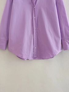 Detail of lavender poplin shirt showing white buttons and curved hem on smooth fabric