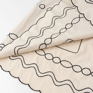 Makrodetail des Wellensaums mit schwarzer Stickerei auf einem beigen Kleid aus Baumwolle