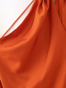 Detail eines orangefarbenen Satinkleides mit elegantem Faltenwurf und feinen Trägern