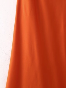 Detail eines orangefarbenen Seidensatin-Neckholder-Kleides mit Fokus auf Stoff und Falten