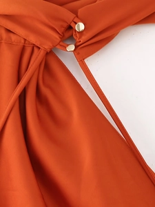Detailansicht eines satinierten Kleides in Orange mit Goldknöpfen und Ausschnitt