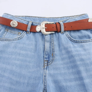Bohemian bruine leren riem met zilveren gegraveerde gesp op een lichtblauwe spijkerbroek