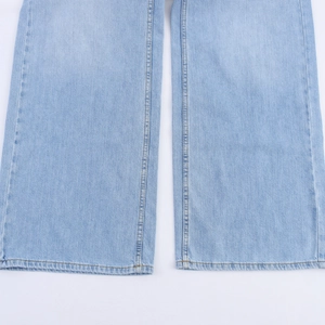 Detailopname van de lichtblauwe denimtextuur en dubbelgestikte zoom op de spijkerbroek