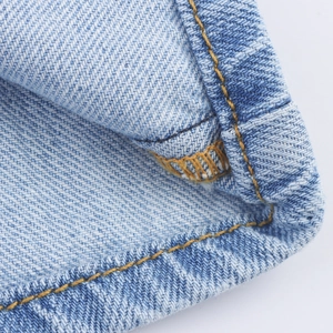 Detailopname van lichtblauwe denim stof met nauwkeurige gele stiksels en afwerking