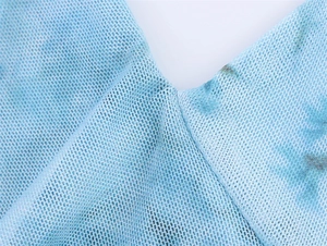 Detail aus hellblauem Mesh-Gewebe mit abstraktem Tie-Dye-Druck und feiner Netzstruktur