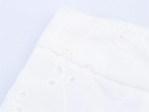 Macro shot of white cotton fabric with intricate eyelet embroidery and detailed stitching