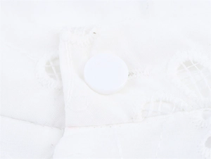 Detailed close-up of white resin button and delicate eyelet embroidery on cotton fabric