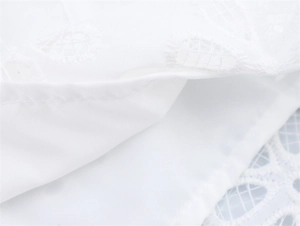 Detailed macro view of white cotton fabric featuring intricate eyelet floral embroidery