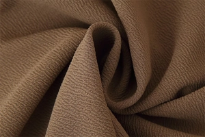 Dettaglio del tessuto marrone scuro con texture granulosa plissettata tipo chiffon