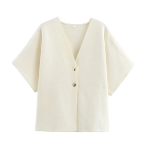 Détail d'un gilet en maille crème avec col en V, boutons dorés et texture de tricot