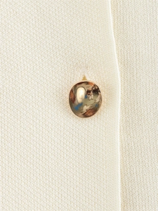 Gros plan d'un bouton métallique doré sur un détail de tricot fin blanc cassé
