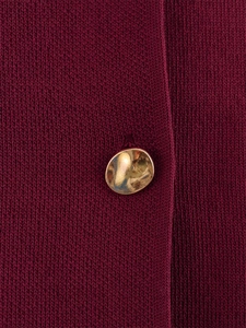 Détail macro de la maille bordeaux avec un bouton métallique doré de forme irrégulière