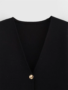 Détail du col en V d'un gilet en maille noire avec un bouton rond doré poli