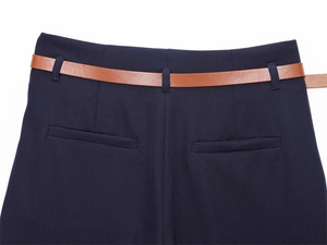 Dettaglio dei pantaloni blu navy che mostra la vita con cintura marrone e tasche a filetto