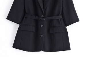 Detail of black short-sleeve blazer featuring a notched lapel and adjustable waist belt
