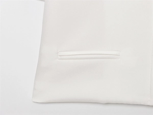 Close-up of a white woven jacket featuring a neatly stitched welt pocket detail