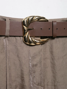 Dettaglio fibbia in metallo dorato su cintura in pelle marrone e pantaloni satin