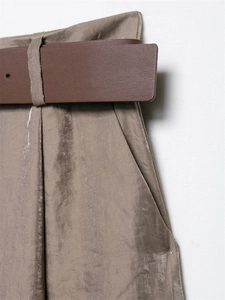 Dettaglio dei pantaloni larghi in satin kaki con pieghe eleganti e cintura in ecopelle marrone