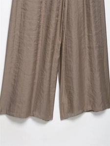 Dettaglio dei pantaloni larghi color talpa con trama setosa e drappeggio elegante
